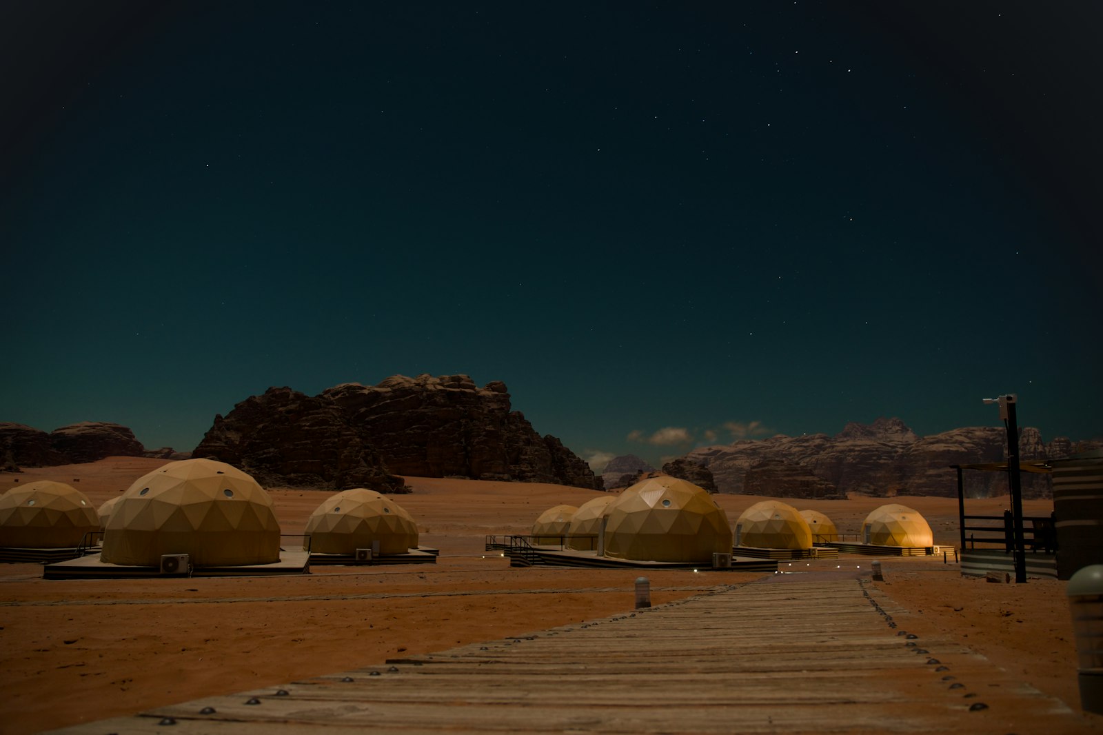 Glowing dome tents of a luxury desert camp under a starry night sky among Wadi Rum's rock formations
